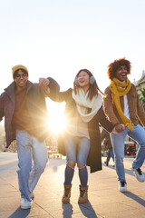 Group of multiracial friends having fun outdoors, walking holding hands and laughing at the city during winter time. - obrazy, fototapety, plakaty