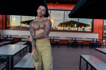 Chico tatuado y musculoso posando sin camiseta en terraza de restaurante de comida rapida