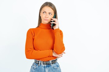 Sad young beautiful girl wearing orange turtleneck talking on smartphone. Communication concept.