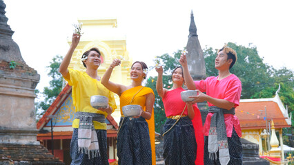 Happy group of young people dressed in traditional Thai clothing are playing in the water during...