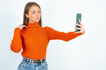 young beautiful caucasian woman wearing orange turtleneck smiling and taking a selfie ready to post...