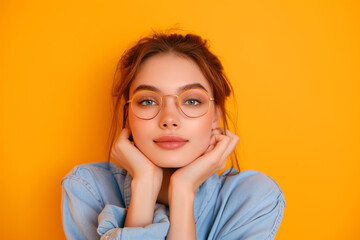 pretty girl in stylish clothes, blue sweater and glasses, arm under chin touch face on yellow color...