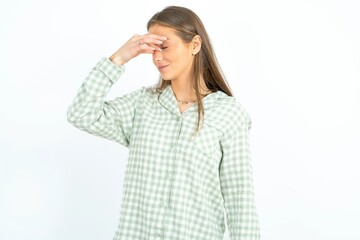 Sad young beautiful woman wearing green plaid pyjama,  suffering from headache holding hand on her...