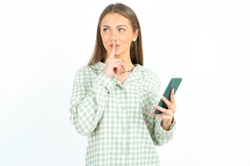 young beautiful woman wearing green plaid pyjama,  holding modern gadget ask not tell secrets