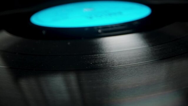 The texture and grooves on the vinyl record that is playing, slowly rotating. Dolly slider, close up.