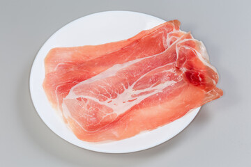 Thin slices of jamon on white dish on gray background