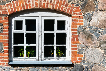 Window with a frame covered with old weathered paint, on a stone wall, framed in red brick. From the windows of the world series.