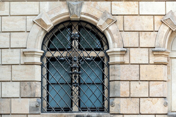 Fototapeta na wymiar Arched window with wrought metal grille with pattern on the background of a beige colored stone block wall. From the windows of the world series.