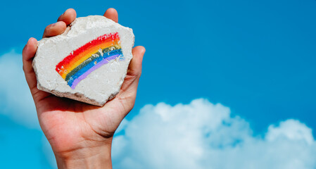 man holds a rock with a rainbow flag painted on it