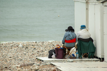 Deux vieilles personnes de dos face à la mer sur plage de galets - 720175555