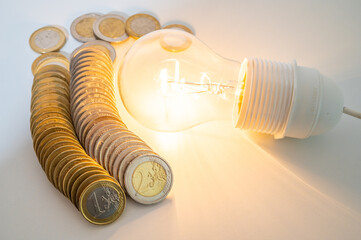 Light bulb lit, with row of coins next to it. Trends in electricity tariffs, energy dependence,...