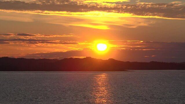 Sunrise or sunset at sea from sundeck of cruise ship. Morning sun, sunbeams and lens flare reflecting on sea surface with calm waves. On the horizon the coast of Norway. Voyage cruise travel concept
