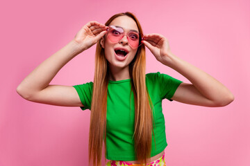 Photo of impressed ecstatic woman with ginger hairdo dressed green t-shirt touching sunglass staring isolated on pink color background