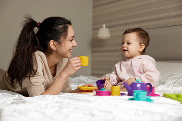 Obraz na płótnie Canvas mother and little child daughter playing tea party and spending time together in bedroom, family having fun
