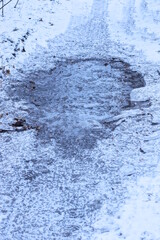frozen puddle with black broken ice in white snow on a winter street