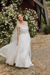 Fototapeta premium Beautiful bride with a long train. The bride in a white dress with a long train in nature on a summer day. Summer wedding.