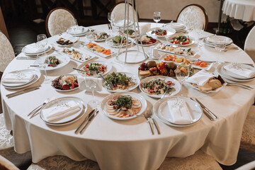 A view of wedding tables, attention to serving, with flower arrangements, expensive cutlery, plates with white napkins.