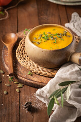Tasty pumpkin cream soup with organic herbs and pumpkin seeds in vintage ceramic bowl