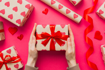 Give a gift on Valentine Day.Valentine gift. Beauty Woman hands holding Gift box with red bow over holiday background