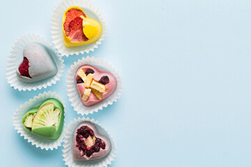 chocolate sweets in the form of a heart with fruits and nuts on a colored background. top view with space for text, holiday concept