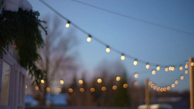 Selective focus shot of outdoor string lights hanging on line on outside house in backyard in cozy evening winter on background of sky. Garden decoration. Party camping. Shooting in slow motion.
