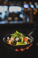 Men's waiter hands hold a Fresh greek salad with tomato, cucumber, bel pepper, olives and feta...