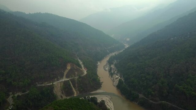 Aerial view above the Tista river, in a valley between mountains and Indian forest, on a sunny day, in Sikkim, India.