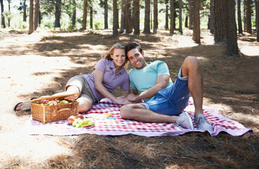Happy couple, picnic portrait and nature with love, romantic celebration and summer date for valentines day. Young people with food, fruits and relax on blanket in woods or forest for anniversary