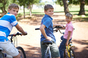 Naklejka premium Nature, happy and portrait of kids on bicycles riding in outdoor field, park or forest for exercise. Smile, cycling and confident young boy children on bikes for cardio, hobby or training in a garden
