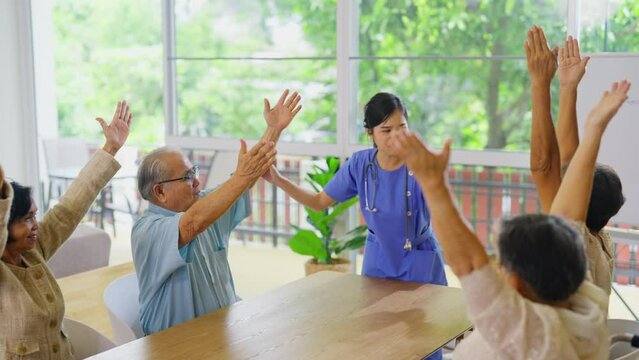 Young Asian nurse stand in front of group of senior or elderly people to show as example for exercise hands in room of clinic or healthcare center.