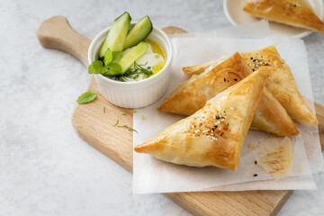 Filo pastry triangle pies and tzatziki dip on wooden board, savory breakfast or appetizer served