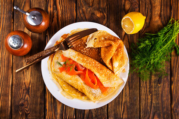 Pancakes with fish salmon, cheese and dill on wooden table