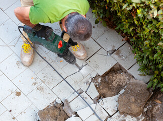 Worker removes garden tiles with jackhammer, top view.
