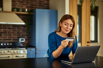 A smiling woman doing an online shopping, holding a credit card, using a laptop.