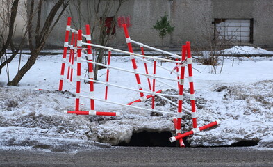 Red and white plastic barriers in the snow protect the site of a small utility accident