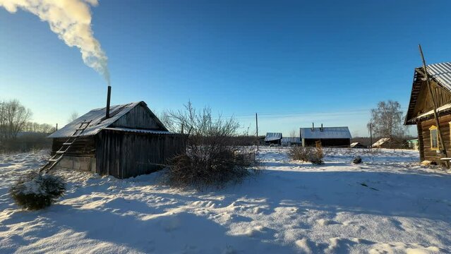 Bathhouse in village in winter time. Smoke from a bathhouse chimney in village. Russian Bath House in countryside. Wooden home in rural in winter. Smoke from Country houses chimney in countryside.