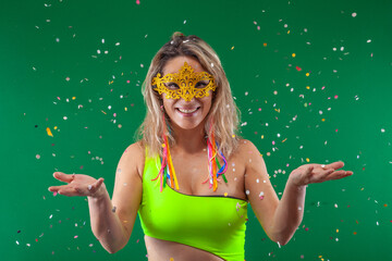 Joyful woman on a green background, wearing colorful clothes, tossing confetti in the air