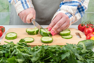 Women's hands chop cucumbers for vegetable salad with a knife.