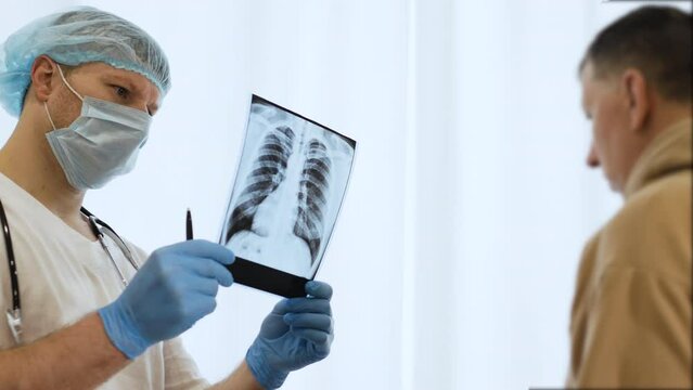 A doctor in an office with a sick patient, a radiographer examines an x-ray of the lungs of an elderly person in a hospital. The doctor diagnoses pneumonia. X-ray in the hands of a male doctor.