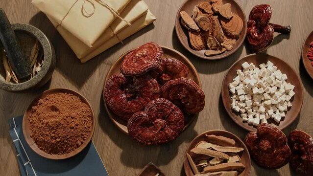 Top view of Ganoderma mushrooms and precious medicinal herbs displayed on wooden plates on the surface of a wooden turntable. Next to them are prescriptions wrapped in kraft paper.