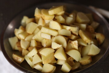 Chopped pieces of potatoes in a steel wok or bowl, under soft light, 