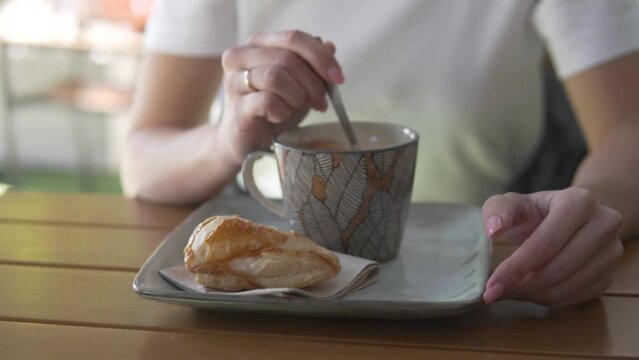 Close-up of a woman's hands stirring in sugar in a cup with a cappuccino