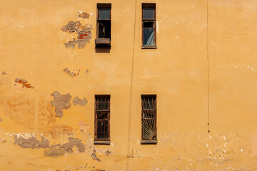 The yellow shabby wall of an old building. Small windows with bars. A sense of abandonment