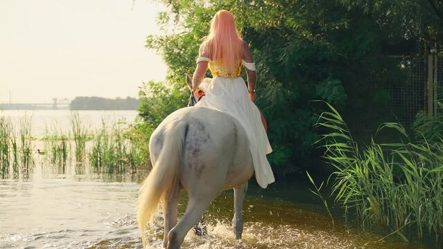 Art video real people Fantasy woman warrior queen sits astride white horse hoof splashes water, greek goddess rides animal walks in river sea lake, sun light sky green tree. elf girl back rear view 4k