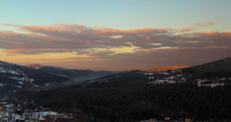 Obraz premium Aerial View of Mountains and Forest Covered with Snow at Sunset in Winter