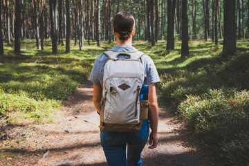A young woman with a backpack walks through the forest. Hiking in the woods. - 720399770
