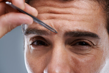 Man, portrait and tweezers for eyebrows in studio or face grooming, hygiene or grey background....