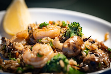 A tightly focused shot capturing the details of a steaming plate of fried rice adorned with shrimp, mushrooms, green peas, broccoli, and topped off with a lemon slice.