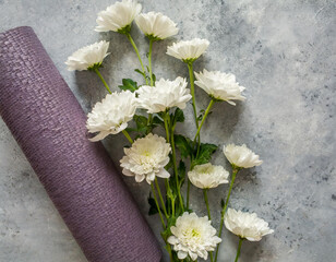 Fototapeta na wymiar Sport background. Rolled yoga mat and beautiful white pastel flowers around. Top view