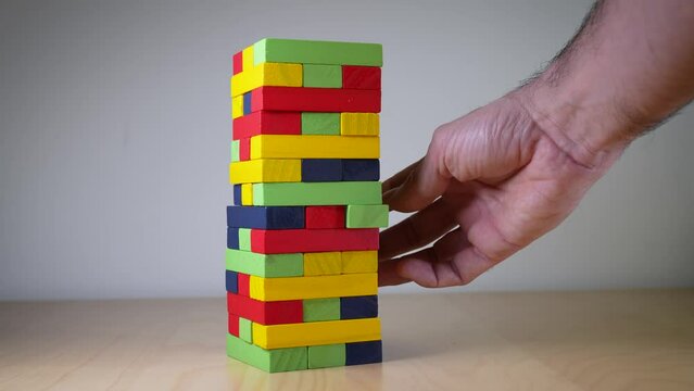 Closeup image of a hand holding and playing Jenga or Tumble tower wooden block game. Suitable for various real life problems or situations, such as Human Resources and employees who support the